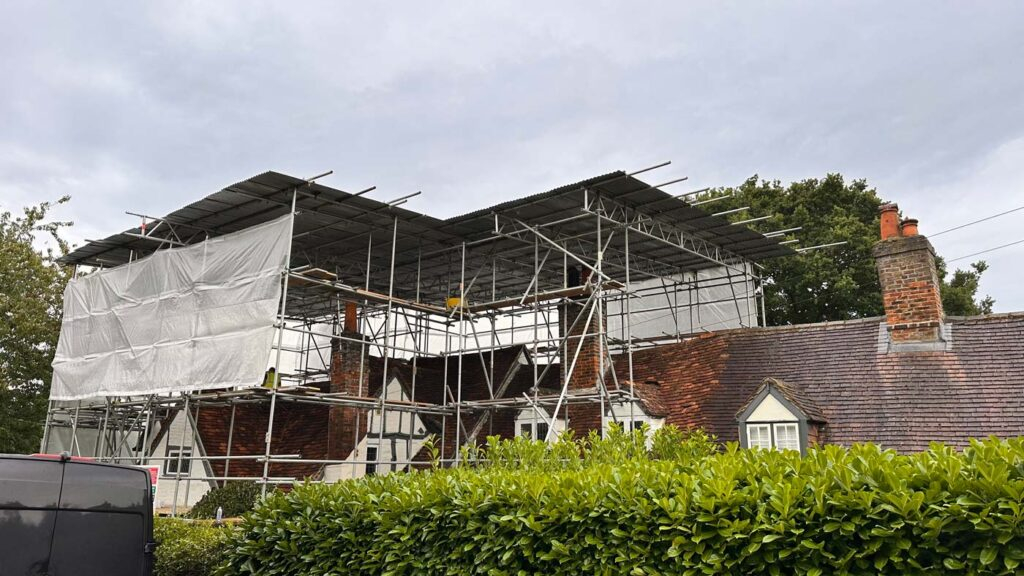 A house with scaffolding on the roof and a van parked in front, undergoing building restoration in Buckinghamshire.